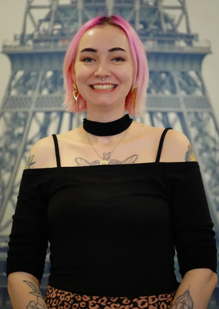 Portrait der Auszubildenden Jenny Haug. Symphatische junge Dame posiert vor einem Poster des Eiffelturms.